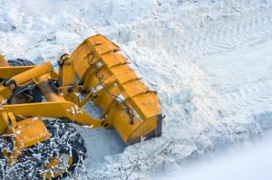 A bulldozer pushing and shoveling snow off of a pathway