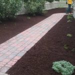 A yard with a red brick pathway and mulched gardens